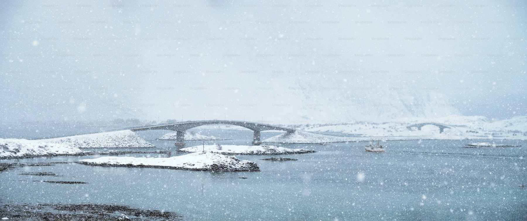 Fishing vessel moving through a snowy Norwegian coastal landscape